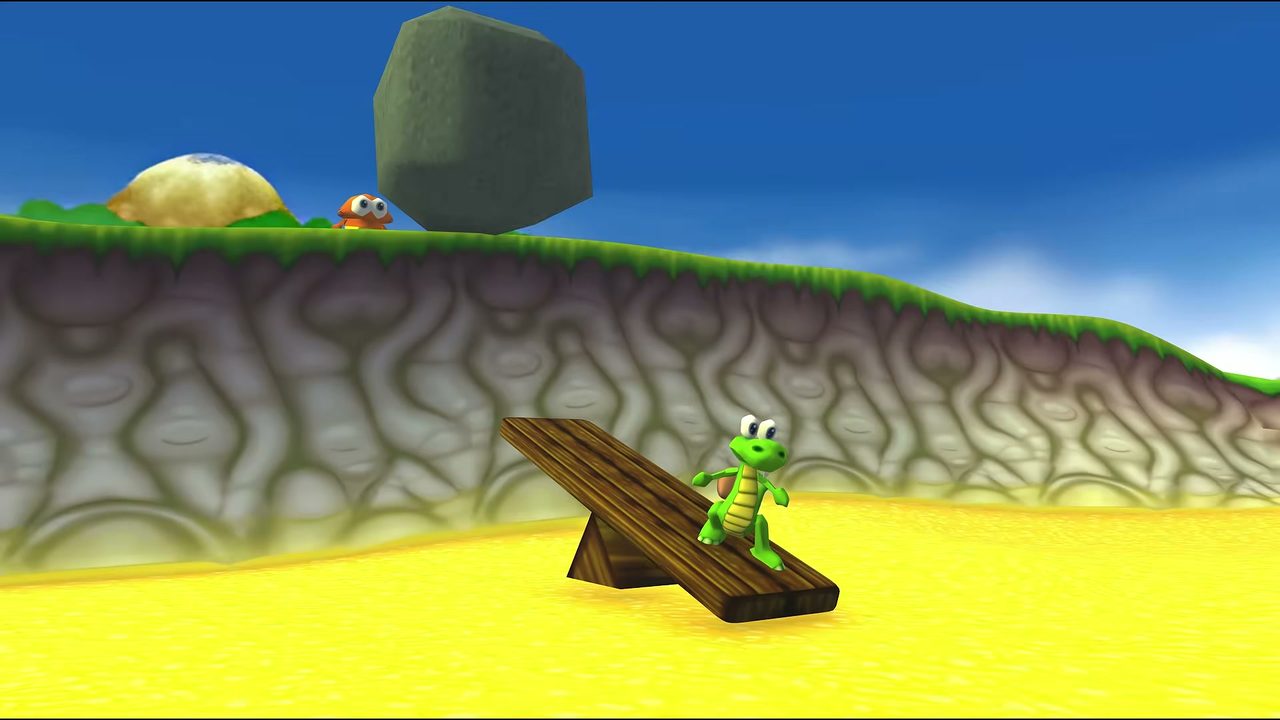 Croc stands on a seesaw plank in a sandy area with a palm tree and a rock behind him